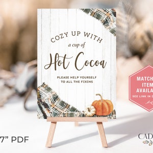Puede incluir: Un caballete de madera muestra un letrero que dice "Cozy up with a cup of Hot Cocoa". El letrero presenta un dise&ntilde;o a cuadros, calabazas y el texto "Please help yourself to all the fixins". Un gr&aacute;fico hexagonal rosa dice "Matching Items Available."
