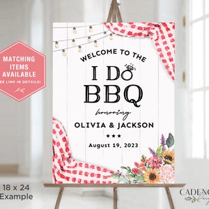 May include: A white wooden sign on an easel with the text "Welcome to the I Do BBQ" honoring Olivia & Jackson, August 19, 2023. The sign is decorated with floral arrangements, string lights, and red and white checkered accents. The sign is 18 x 24 inches.
