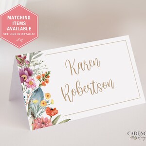 Puede incluir: Una tarjeta de lugar blanca con un dise&ntilde;o floral en el lado izquierdo y el nombre "Karen Robertson" escrito en cursiva marr&oacute;n en el lado derecho.