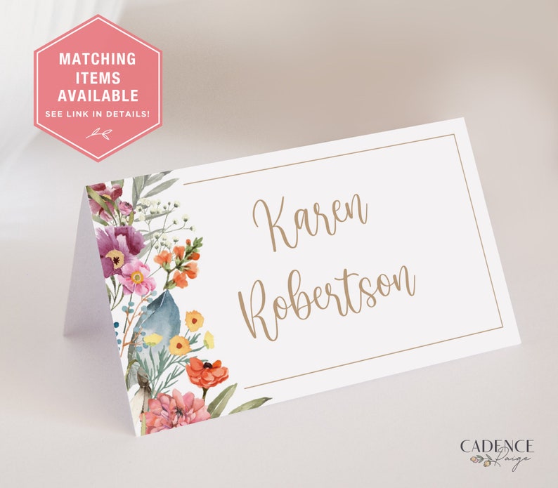Puede incluir: Una tarjeta de lugar blanca con un dise&ntilde;o floral en el lado izquierdo y el nombre "Karen Robertson" escrito en cursiva marr&oacute;n en el lado derecho.