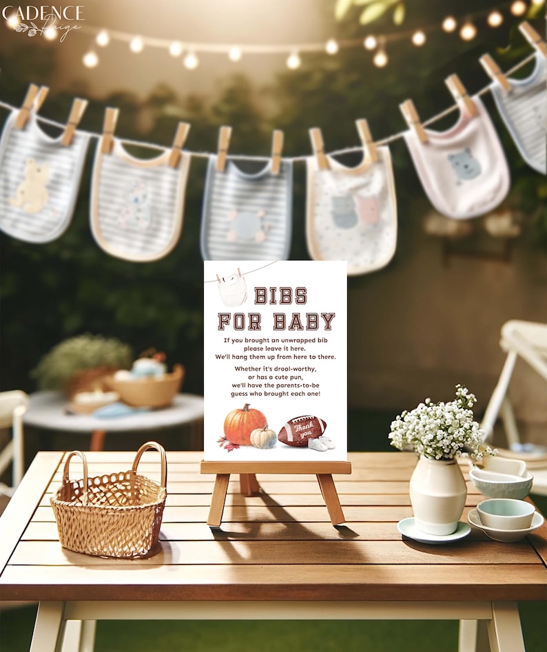 K&ouml;nnte beinhalten: Ein wei&szlig;es Schild mit braunem Text, auf dem "Bibs for Baby" steht. Das Schild steht auf einem Holzstaffelei und hat ein Herbstthema mit K&uuml;rbissen und einem Fu&szlig;ball. Das Schild steht auf einem Holztisch mit einem Weidenkorb, einer Vase mit wei&szlig;en Blumen und zwei kleinen wei&szlig;en Tassen.