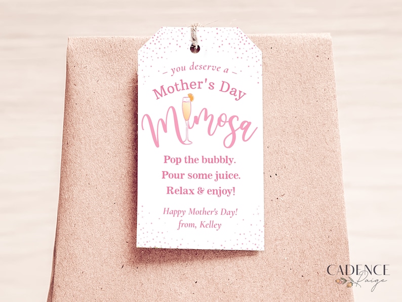 Pu&ograve; includere: Etichetta regalo rosa con pois bianchi e il testo "you deserve a Mother's Day Mimosa" con un'illustrazione rosa di una bevanda mimosa. L'etichetta include anche il testo "Pop the bubbly. Pour some juice. Relax & enjoy! Happy Mother's Day! from, Kelley"