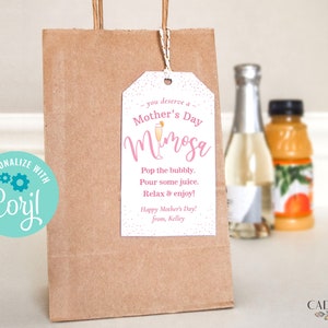 Pu&ograve; includere: Un'etichetta regalo rosa e bianca con il testo "you deserve a Mother's Day Mimosa" e istruzioni per "Pop the bubbly. Pour some juice. Relax & enjoy!" L'etichetta &egrave; legata con uno spago a un sacchetto di carta marrone.