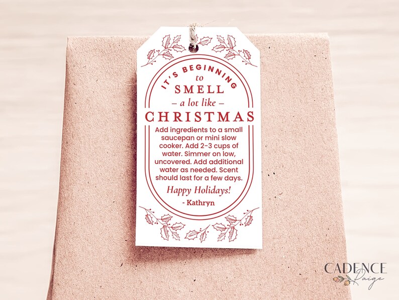 May include: A white gift tag with red text that reads "It's beginning to smell - a lot like - Christmas". The tag includes instructions for making a Christmas potpourri, "Add ingredients to a small saucepan or mini slow cooker. Add 2-3 cups of water. Simmer on low, uncovered. Add additional water as needed. Scent should last for a few days. Happy Holidays! - Kathryn".