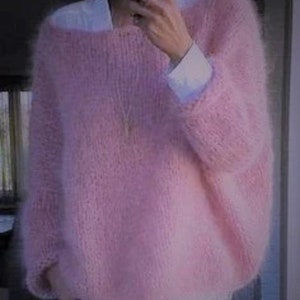 Puede incluir: Un suéter suave y peludo de color rosa con mangas largas y cuello redondo.