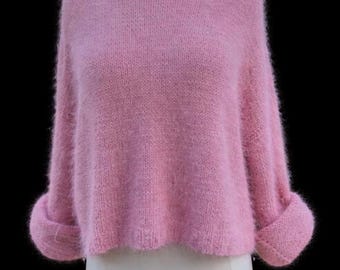 Può includere: Un maglione rosa chiaro, soffice, a maniche lunghe con un ampio scollo rotondo e maniche con risvolto. Il capo presenta una consistenza morbida e spazzolata e una lunghezza corta, esposto su un manichino su sfondo nero.
