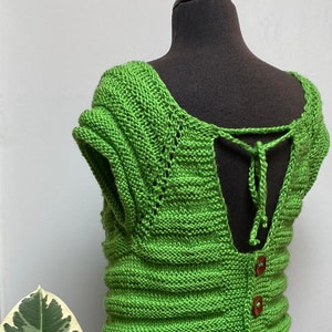 以下が含まれることがあります： 緑色のニットトップで、背中は低く、リボンで結ぶことができます。トップはリブ編みで、袖は短いです。前面には木製のボタンが3つ付いています。