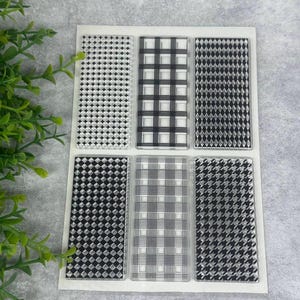 Könnte beinhalten: Ein Set aus sechs rechteckigen Stempeln mit verschiedenen schwarz-weißen Mustern. Die Muster umfassen Diamanten, Karos und Hahnentritt-Designs. Die Stempel sind auf einem weißen Träger angeordnet, ideal für Bastel- und Scrapbooking-Projekte.