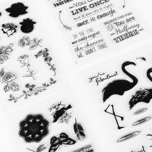 May include: Clear stamps featuring floral designs, butterflies, and flamingos. Text includes phrases like "Live Once" and "You're Fabulous!" The stamps are in black and white, ideal for crafting and scrapbooking projects.
