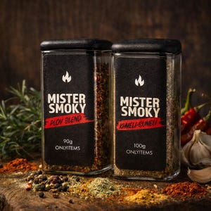 Może przedstawiać: Dwa szklane słoiki z przyprawami z czarnymi wieczkami i etykietami z napisem "Mister Smoky". Jeden słoik jest oznaczony "Plov Blend" i zawiera 90g przypraw. Drugi jest oznaczony "Khmeli-Suneli" i zawiera 100g przypraw. Słoiki stoją na drewnianej powierzchni.