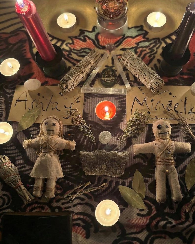 May include: An overhead shot of a spiritual altar with candles, sage bundles, and voodoo dolls. The scene includes lit candles, dried herbs, and two dolls with pins. The names "Ashla" and "Michael" are written on paper.