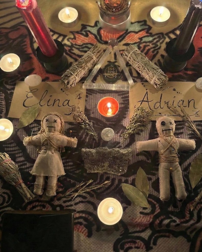 May include: An overhead shot of a spiritual altar with candles, sage bundles, and two voodoo dolls. The names "Elina" and "Adrian" are written on parchment. A triangular glass piece with text is centered above a lit candle.