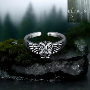 Peut inclure: Une bague ouverte en métal argenté représentant un hibou aux ailes déployées. Le hibou présente des yeux saillants et des détails de plumes texturés sur le corps et les ailes. La bague est ajustable pour s'adapter à différentes tailles.