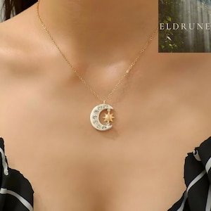 Può includere: Una collana a catena color oro con un ciondolo a forma di mezzaluna incastonato di cristalli trasparenti e una piccola stella centrale color oro. L'immagine include il testo ELDRUNE nell'angolo in alto a destra su uno sfondo boschivo.