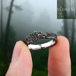 May include: A silver-toned metal ring featuring a detailed wolf head design with textured fur detailing. The band is polished on the interior and has a dark, oxidised finish on the exterior surface. The word ELDRUNE is visible in the top corner.