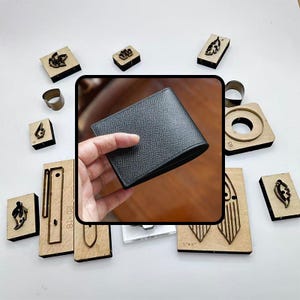 Puede incluir: Una cartera de cuero negro se sostiene en una mano, rodeada de varias herramientas de artesanía de madera y metal. La cartera tiene una superficie texturizada. Las herramientas incluyen sellos con diseños de hojas y geométricos, y anillos de metal.