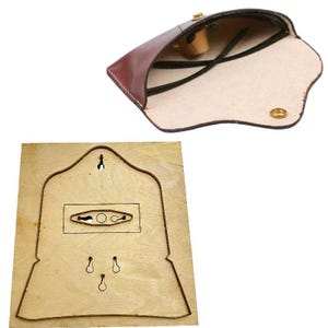 May include: A burgundy leather eyeglass case with a gold clasp, open to reveal black-framed glasses. Below, a wooden die with a cut-out pattern for crafting leather goods, likely for the case.