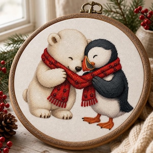 Puede incluir: Un bastidor de bordado circular de madera que contiene un diseño de punto de cruz de un oso polar color crema y un frailecillo blanco y negro. Ambos animales están envueltos juntos en una larga bufanda roja con un pequeño patrón oscuro.