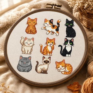 Puede incluir: Un bastidor de bordado circular de madera que contiene un panel de tela blanca con un patrón de punto de cruz de nueve gatos distintos. Los gatos incluyen variedades atigradas naranjas, calicó, negras, grises, siamesas y esmoquin.