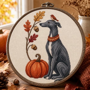 May include: A circular embroidery hoop containing a cross-stitch design of a grey dog wearing a red patterned collar, sitting next to a large orange pumpkin. A small bird rests on the dog's head, and a branch with autumn leaves and acorns.