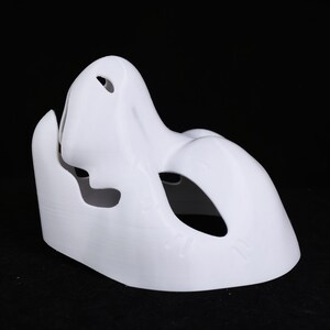 May include: A white sculpted mask with a human-like form. The mask has eye and mouth openings, and a prominent nose and cheekbone structure. The mask is made of a smooth, solid material against a black background.
