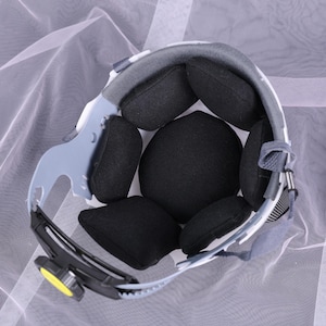 May include: Interior view of a safety helmet, showcasing its internal components. The helmet features a white and gray outer shell, with black padded cushions for comfort and impact absorption. A gray suspension system and a yellow adjustment knob are visible.