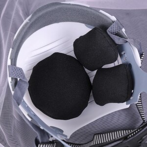 May include: Close-up of the interior of a white safety helmet with black padding. The helmet has a gray rim and adjustable straps. The image is well-lit, showing the details of the protective gear.