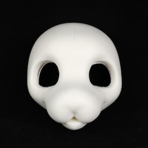 May include: A blank, white, animal-shaped mask with large eye openings and a rounded snout. The mask is smooth and appears to be made of a solid material. The background is black.