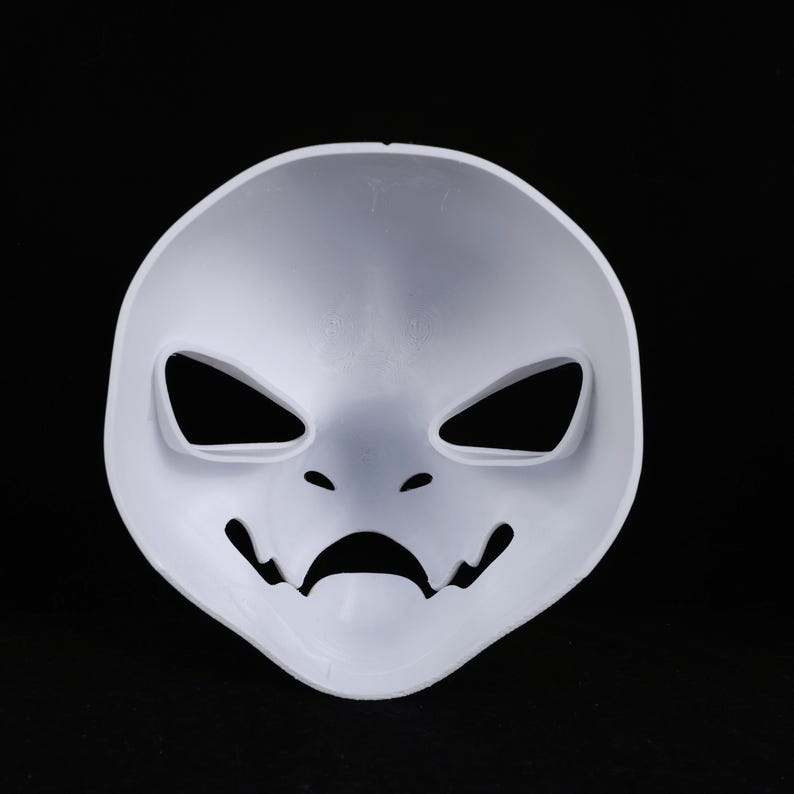 May include: A plain white mask with a simplified face design. It has angular eye cutouts, small holes for nostrils, and a curved mouth with jagged edges. The mask is made of a smooth, solid material.