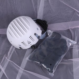 May include: A white helmet with black accents and a clear plastic bag containing black items. The helmet has a series of vertical vents and a strap. The items in the bag are black and appear to be protective gear.