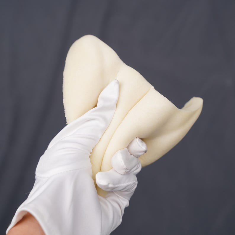 May include: A soft, off-white, curved foam piece with a smooth texture. The object is pliable and features a rounded, organic shape that tapers toward the edges, showing a consistent matte finish across its entire surface area.