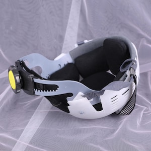 May include: White and gray safety helmet with a black adjustment knob and black interior padding. The helmet has a gray strap and a black and white striped chin strap. The interior has black padding for comfort.