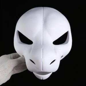 May include: A white mask with a dragon-like design. The mask has large, angled eye openings, small nostril holes, and a slightly open mouth. The mask is held by a gloved hand against a black background.