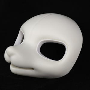 Puede incluir: Una máscara en blanco roto con forma de cabeza de animal, con grandes aberturas para los ojos y un hocico prominente. La máscara es lisa y parece estar hecha de un material sólido, posiblemente plástico o resina. El diseño sugiere que es para disfraces o cosplay.