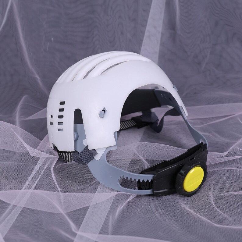 May include: A white safety helmet with a curved design and ventilation slots. The helmet has a gray and black adjustable chin strap with a yellow dial. The helmet is designed for head protection.