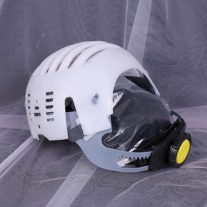 May include: White safety helmet with a vented top, gray chin guard, and a black and yellow adjustment dial. The helmet appears to have a clear face shield and a gray strap.