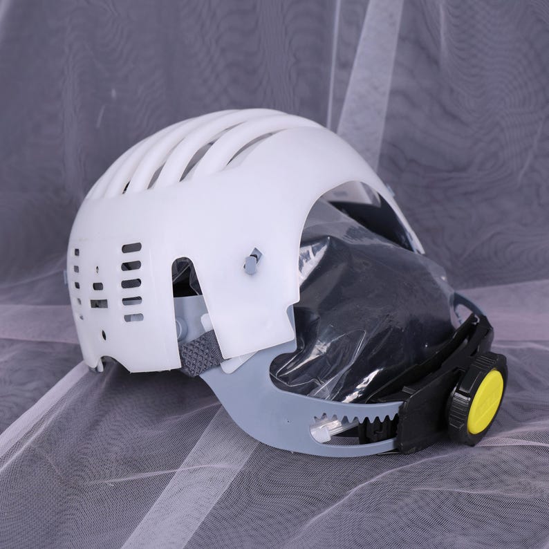 May include: White safety helmet with a vented top, gray chin guard, and a black and yellow adjustment dial. The helmet appears to have a clear face shield and a gray strap.