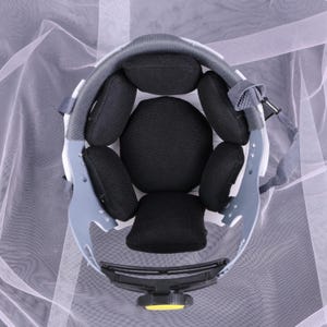 May include: An overhead view of the interior of a white and gray safety helmet. The helmet features black padding and a yellow adjustment knob. The design includes a gray suspension system and a chin strap.