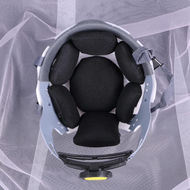 May include: An overhead view of the interior of a white and gray safety helmet. The helmet features black padding and a yellow adjustment knob. The design includes a gray suspension system and a chin strap.