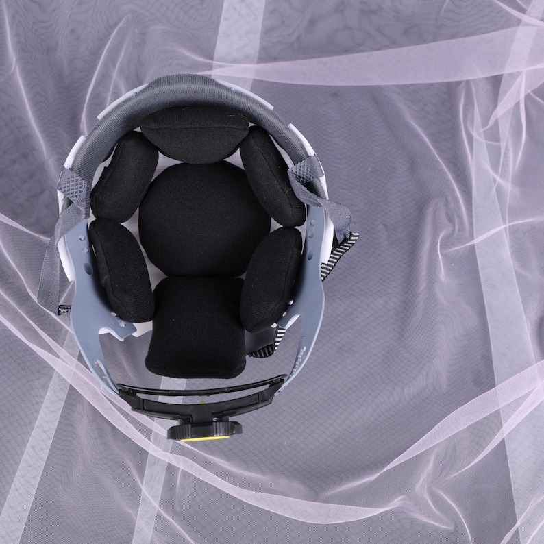 May include: An overhead view of a gray and white helmet with black padding. The helmet has a black adjustment knob and gray straps. The interior padding is black and designed for comfort. The helmet is designed for safety and protection.