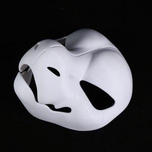 May include: A white plastic mask with eye and mouth cutouts. The mask has a smooth, curved design and is intended to cover the face. It is likely for costume or theatrical purposes.