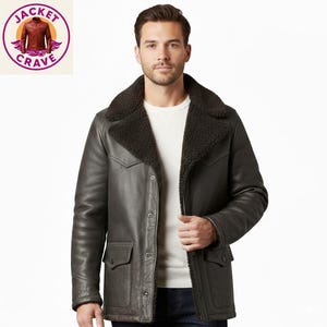 Puede incluir: Chaqueta de cuero gris oscuro con cuello y forro de borrego negro. La chaqueta tiene dos bolsillos delanteros y cierre de botones. Un logotipo es visible en la esquina superior izquierda. Estilo clásico.