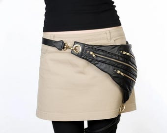May include: Black leather fanny pack with three zipped compartments and gold-coloured hardware. The belt is black leather with a gold-coloured buckle. The fanny pack is worn around the waist over a beige skirt.