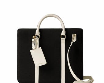 May include: Black rectangular tote bag with white detailing, a top handle, and a detachable shoulder strap. The bag includes a white luggage tag with the brand name "SORILA". The bag has a minimalist design.