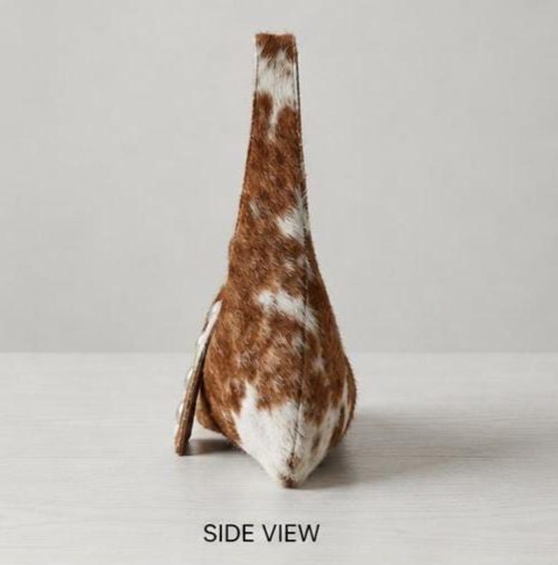 Brown and white cowhide hobo bag with curved shoulder strap and pearl snap button trim, hair-on-hide leather purse for western boho style, shown on a light wood tabletop.