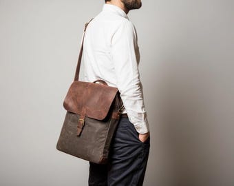 May include: A brown and olive green messenger bag with a leather flap and shoulder strap. The bag has a buckle closure and a handle on top. The bag is carried over the shoulder.