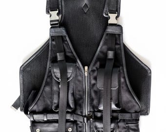 May include: Black leather tactical vest featuring multiple pockets, straps, and metal buckles. The vest has a mesh back panel and a front zip closure. The design includes adjustable straps and various compartments for storage.