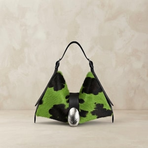May include: A structured handbag featuring a vibrant lime green and black cowhide pattern. The bag has a triangular silhouette, a black leather handle, and a prominent, smooth, oval-shaped silver-toned metal accent centred on the front closure.