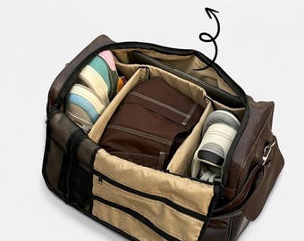 May include: Open brown leather travel bag with multiple compartments. The bag contains clothing, shoes, and a laptop. The text "Padded Laptop Compartment" is above the bag.