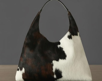 May include: A cowhide shoulder bag with a black leather strap. The bag has a pattern of black, brown, and white fur. The bag's design is a stylish, everyday accessory.